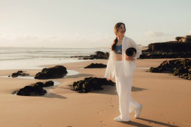 Okyanus kıyısında yoga minderli beyaz elbiseli Asyalı mutlu kadın. Sağlık egzersizleri ve yoga kavramı. Sadece turizm. Dizinin bir parçası.