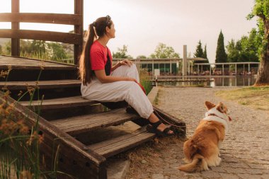 Güneşli bir günde parkta Galli Corgi 'yle bir kadının yakın çekimi. Hayvan bakımı ve arkadaşlık kavramı. Köpek gezdirici. Evcil hayvanıyla sabah yürüyüşünde eğlenen bir kadın. Yumuşak odaklanma. Bir serinin parçası.