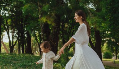 Güneşli bir parkta bebeğiyle çimlerin üzerinde oynayan mutlu genç bir anne. Aile bağları, erken öğrenme, ebeveynlik, aşk, açık hava yaşam tarzı, çocukluk gelişimi, otantik gerçek yaşam anı. Bir serinin parçası.