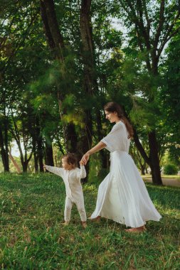 Güneşli bir parkta bebeğiyle çimlerin üzerinde oynayan mutlu genç bir anne. Aile bağları, erken öğrenme, ebeveynlik, aşk, açık hava yaşam tarzı, çocukluk gelişimi, otantik gerçek yaşam anı. Bir serinin parçası.