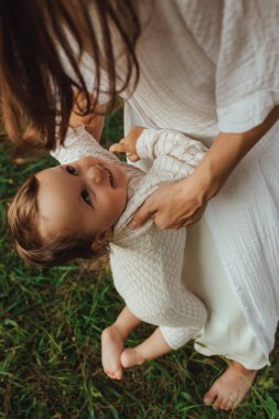 Güneşli bir parkta bebeğiyle çimlerin üzerinde oynayan mutlu genç bir anne. Aile bağları, erken öğrenme, ebeveynlik, aşk, açık hava yaşam tarzı, çocukluk gelişimi, otantik gerçek yaşam anı. Bir serinin parçası.