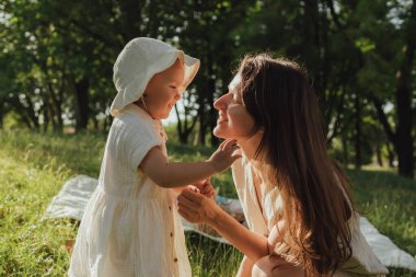 Güneşli bir parkta bebeğiyle çimlerin üzerinde oynayan mutlu genç bir anne. Aile bağları, erken öğrenme, ebeveynlik, aşk, açık hava yaşam tarzı, çocukluk gelişimi, otantik gerçek yaşam anı. Bir serinin parçası.