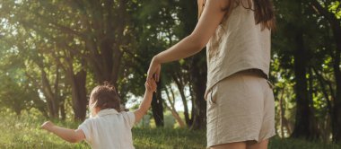 Güneşli bir parkta bebeğiyle çimlerin üzerinde oynayan mutlu genç bir anne. Aile bağları, erken öğrenme, ebeveynlik, aşk, açık hava yaşam tarzı, çocukluk gelişimi, otantik gerçek yaşam anı. Bir serinin parçası.