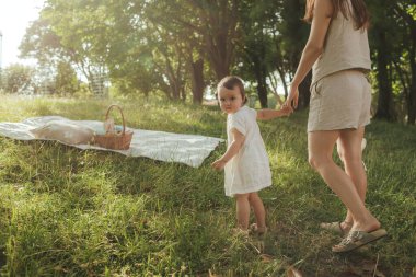 Güneşli bir parkta bebeğiyle çimlerin üzerinde oynayan mutlu genç bir anne. Aile bağları, erken öğrenme, ebeveynlik, aşk, açık hava yaşam tarzı, çocukluk gelişimi, otantik gerçek yaşam anı. Bir serinin parçası.
