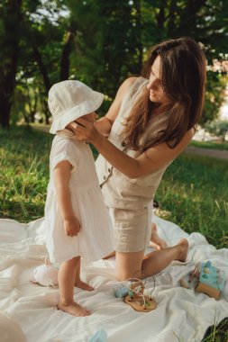 Güneşli bir parkta bebeğiyle çimlerin üzerinde oynayan mutlu genç bir anne. Aile bağları, erken öğrenme, ebeveynlik, aşk, açık hava yaşam tarzı, çocukluk gelişimi, otantik gerçek yaşam anı. Bir serinin parçası.
