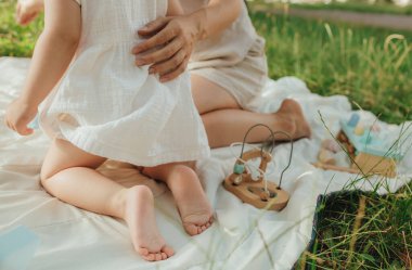 Güneşli bir parkta bebeğiyle çimlerin üzerinde oynayan mutlu genç bir anne. Aile bağları, erken öğrenme, ebeveynlik, aşk, açık hava yaşam tarzı, çocukluk gelişimi, otantik gerçek yaşam anı. Bir serinin parçası.