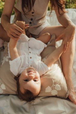 Güneşli bir parkta bebeğiyle çimlerin üzerinde oynayan mutlu genç bir anne. Aile bağları, erken öğrenme, ebeveynlik, aşk, açık hava yaşam tarzı, çocukluk gelişimi, otantik gerçek yaşam anı. Bir serinin parçası.