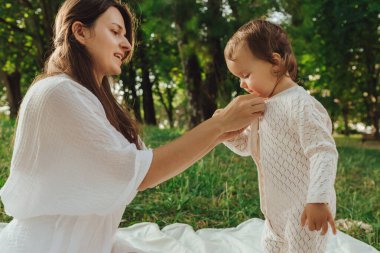Güneşli bir parkta bebeğiyle çimlerin üzerinde oynayan mutlu genç bir anne. Aile bağları, erken öğrenme, ebeveynlik, aşk, açık hava yaşam tarzı, çocukluk gelişimi, otantik gerçek yaşam anı. Bir serinin parçası.