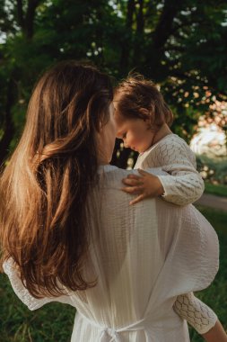 Güneşli bir parkta bebeğiyle çimlerin üzerinde oynayan mutlu genç bir anne. Aile bağları, erken öğrenme, ebeveynlik, aşk, açık hava yaşam tarzı, çocukluk gelişimi, otantik gerçek yaşam anı. Bir serinin parçası.