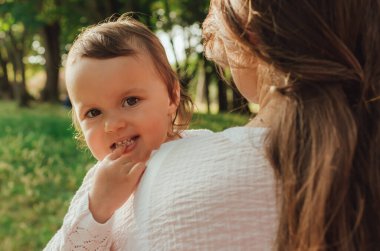 Güneşli bir parkta bebeğiyle çimlerin üzerinde oynayan mutlu genç bir anne. Aile bağları, erken öğrenme, ebeveynlik, aşk, açık hava yaşam tarzı, çocukluk gelişimi, otantik gerçek yaşam anı. Bir serinin parçası.