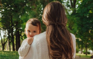 Güneşli bir parkta bebeğiyle çimlerin üzerinde oynayan mutlu genç bir anne. Aile bağları, erken öğrenme, ebeveynlik, aşk, açık hava yaşam tarzı, çocukluk gelişimi, otantik gerçek yaşam anı. Bir serinin parçası.