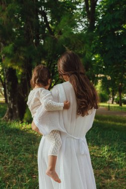Güneşli bir parkta bebeğiyle çimlerin üzerinde oynayan mutlu genç bir anne. Aile bağları, erken öğrenme, ebeveynlik, aşk, açık hava yaşam tarzı, çocukluk gelişimi, otantik gerçek yaşam anı. Bir serinin parçası.