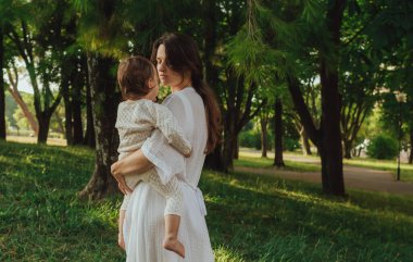 Güneşli bir parkta bebeğiyle çimlerin üzerinde oynayan mutlu genç bir anne. Aile bağları, erken öğrenme, ebeveynlik, aşk, açık hava yaşam tarzı, çocukluk gelişimi, otantik gerçek yaşam anı. Bir serinin parçası.