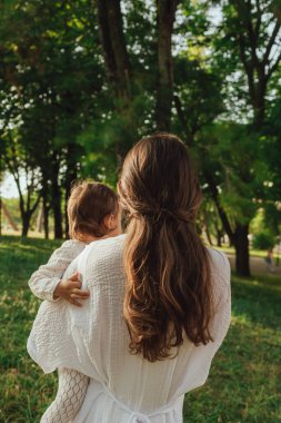 Güneşli bir parkta bebeğiyle çimlerin üzerinde oynayan mutlu genç bir anne. Aile bağları, erken öğrenme, ebeveynlik, aşk, açık hava yaşam tarzı, çocukluk gelişimi, otantik gerçek yaşam anı. Bir serinin parçası.