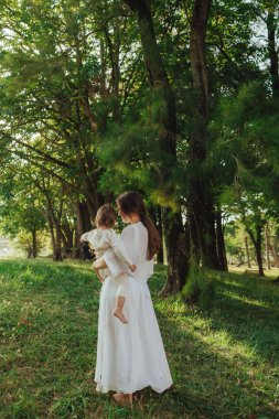 Güneşli bir parkta bebeğiyle çimlerin üzerinde oynayan mutlu genç bir anne. Aile bağları, erken öğrenme, ebeveynlik, aşk, açık hava yaşam tarzı, çocukluk gelişimi, otantik gerçek yaşam anı. Bir serinin parçası.