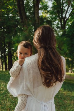 Güneşli bir parkta bebeğiyle çimlerin üzerinde oynayan mutlu genç bir anne. Aile bağları, erken öğrenme, ebeveynlik, açık hava yaşam tarzı, çocukluk gelişimi, otantik gerçek yaşam anı. Bir serinin parçası