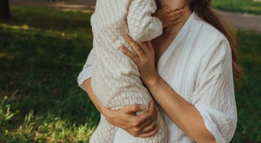 Güneşli bir parkta bebeğiyle çimlerin üzerinde oynayan mutlu genç bir anne. Aile bağları, erken öğrenme, ebeveynlik, açık hava yaşam tarzı, çocukluk gelişimi, otantik gerçek yaşam anı. Bir serinin parçası