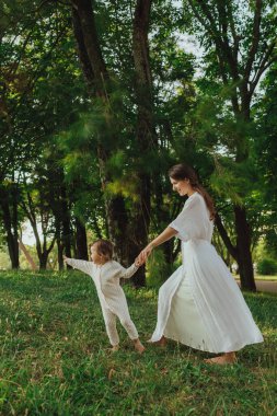 Güneşli bir parkta bebeğiyle çimlerin üzerinde oynayan mutlu genç bir anne. Aile bağları, erken öğrenme, ebeveynlik, açık hava yaşam tarzı, çocukluk gelişimi, otantik gerçek yaşam anı. Bir serinin parçası