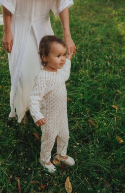 Güneşli bir parkta bebeğiyle çimlerin üzerinde oynayan mutlu genç bir anne. Aile bağları, erken öğrenme, ebeveynlik, açık hava yaşam tarzı, çocukluk gelişimi, otantik gerçek yaşam anı. Bir serinin parçası