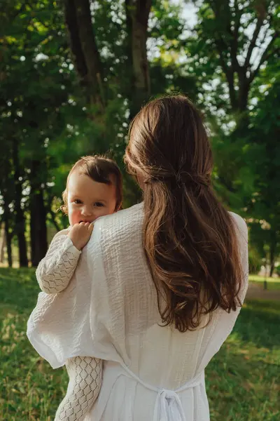 Güneşli bir parkta bebeğiyle çimlerin üzerinde oynayan mutlu genç bir anne. Aile bağları, erken öğrenme, ebeveynlik, açık hava yaşam tarzı, çocukluk gelişimi, otantik gerçek yaşam anı. Bir serinin parçası