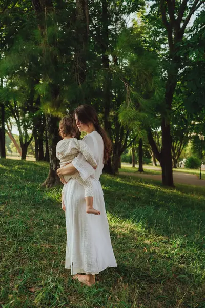 Güneşli bir parkta bebeğiyle çimlerin üzerinde oynayan mutlu genç bir anne. Aile bağları, erken öğrenme, ebeveynlik, açık hava yaşam tarzı, çocukluk gelişimi, otantik gerçek yaşam anı. Bir serinin parçası