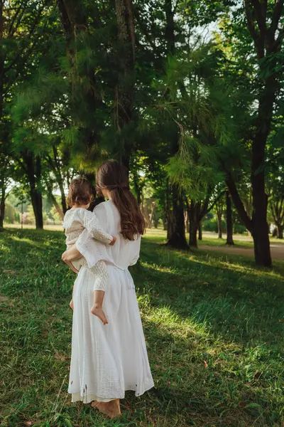 Güneşli bir parkta bebeğiyle çimlerin üzerinde oynayan mutlu genç bir anne. Aile bağları, erken öğrenme, ebeveynlik, açık hava yaşam tarzı, çocukluk gelişimi, otantik gerçek yaşam anı. Bir serinin parçası