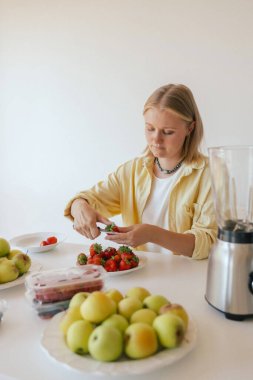Beyaz kadın ev yapımı meyve derisi hazırlıyor, sağlıklı bir atıştırmalık için mutfağında taze meyve dilimliyor. Organik ikramlar ve doğal yaşam üzerine bir dizi..