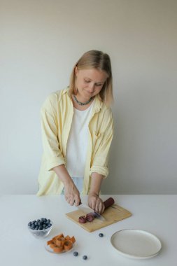 Beyaz kadın ev yapımı meyve derisi hazırlıyor, sağlıklı bir atıştırmalık için mutfağında taze meyve dilimliyor. Organik ikramlar ve doğal yaşam üzerine bir dizi..