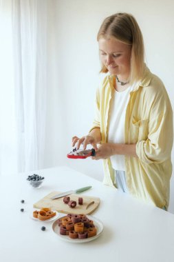 Orta yaşlı bir kadın ev yapımı meyve derisi hazırlıyor, sağlıklı bir atıştırmalık için mutfağında taze meyve dilimliyor. Organik ikramlar ve doğal yaşam üzerine bir serinin parçası. Kullanıcı tarafından oluşturulan içerik.