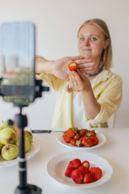 Orta yaşlı bir kadın ev yapımı meyve derisi hazırlıyor. Mutfağında taze meyve dilimleyip sağlıklı bir şeyler atıştırıyor ve telefonundan yayın yapıyor. Dizinin bir parçası. Kullanıcı tarafından oluşturulan içerik.