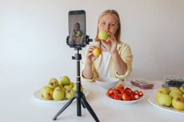 Orta yaşlı bir kadın ev yapımı meyve derisi hazırlıyor. Mutfağında taze meyve dilimleyip sağlıklı bir şeyler atıştırıyor ve telefonundan yayın yapıyor. Dizinin bir parçası. Kullanıcı tarafından oluşturulan içerik.