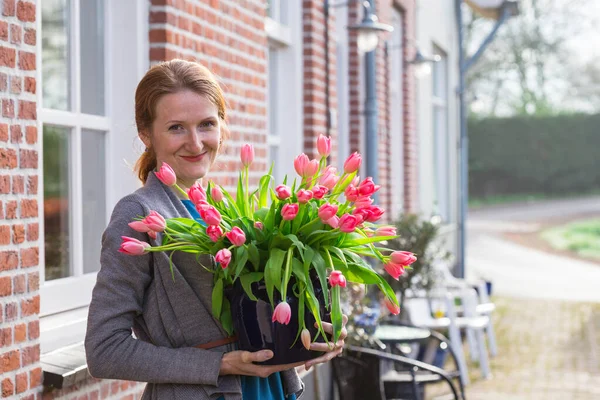 stock image smiling happy girl holding a vase with pink tulips near with a traditional Dutch house. The Netherland