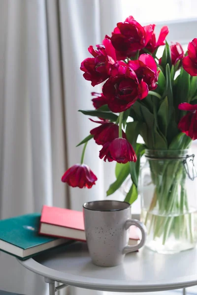 カップと本の入った花瓶の美しいピンクのチューリップはまだ半分 — ストック写真