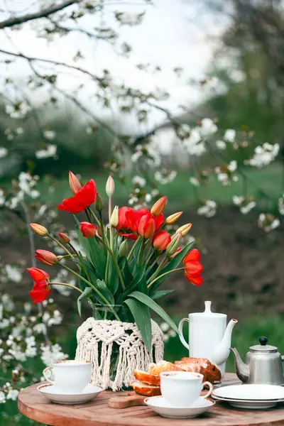 田舎風の庭とお茶会 静物画 カップ ケーキ 赤いチューリップの花瓶 ストックフォト