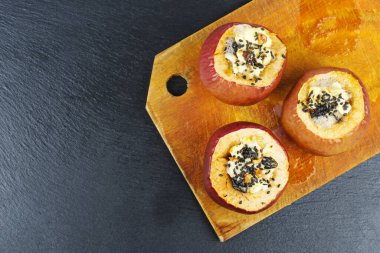 Siyah taş zemin üzerinde sezame tohumları ve ceviz ile doldurulmuş fırında elmalar