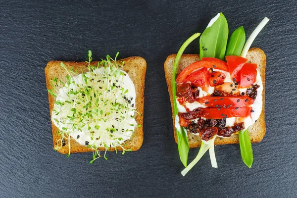 緑のアルファルファの芽 黒石スレートの背景に全粒粉パンのトーストスライスに新鮮な乾燥トマト — ストック写真