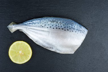 Pişirmeye hazır taze pompano balığı limon dilimi siyah taştan bir arka planda