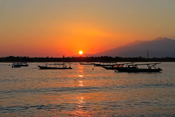 Scenic beach with boats silhouetted at sunset on a tropical island of Indonesia