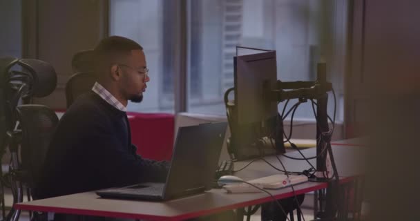 若いアフリカ系アメリカ人のビジネスマンや現代の同僚のオフィスに座って コンピュータで働く眼鏡を持つソフトウェアエンジニア 高品質の写真 — ストック動画