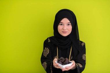Ramazan ayının iftar saatinde elinde tatlı tarihlerle dolu bir tabak tutan modern Müslüman kadın İslami sağlıklı gıda kavramı UFO yeşil arka planda. Yüksek kalite fotoğraf