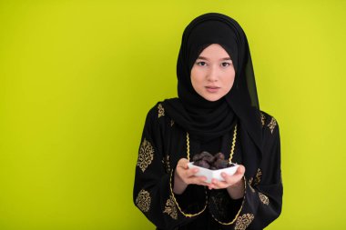 Ramazan ayının iftar saatinde elinde tatlı tarihlerle dolu bir tabak tutan modern Müslüman kadın İslami sağlıklı gıda kavramı UFO yeşil arka planda. Yüksek kalite fotoğraf