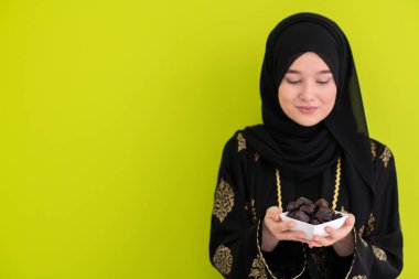 Ramazan ayının iftar saatinde elinde tatlı tarihlerle dolu bir tabak tutan modern Müslüman kadın İslami sağlıklı gıda kavramı UFO yeşil arka planda. Yüksek kalite fotoğraf