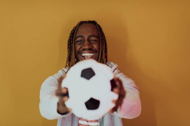 Elinde futbol topu tutarken sarı arka planda poz veren Afro bir adam. Yüksek kalite fotoğraf