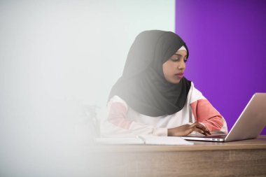 Başörtüsü takan Afro bir kadın özenle evinde oturuyor ve dizüstü bilgisayar ve akıllı telefon kullanıyor. Yüksek kalite fotoğraf