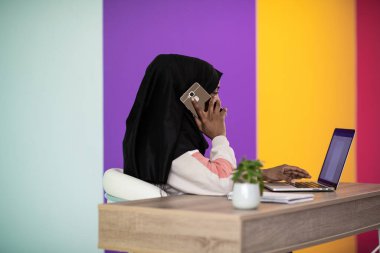 Başörtüsü takan Afro bir kadın özenle evinde oturuyor ve dizüstü bilgisayar ve akıllı telefon kullanıyor. Yüksek kalite fotoğraf