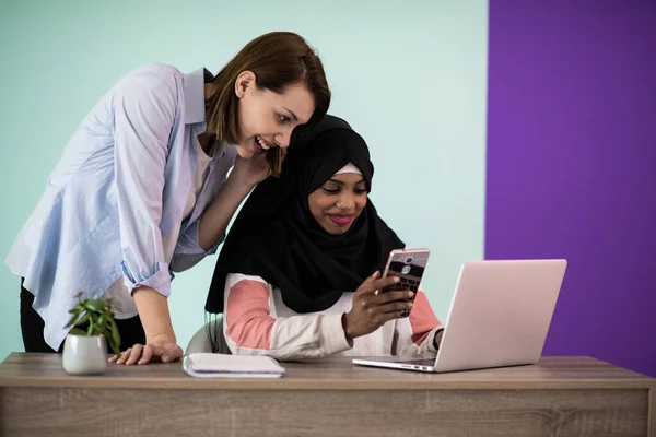 stock image Afro woman with a hijab and a European woman using a smartphone and laptop in their home office. High quality photo