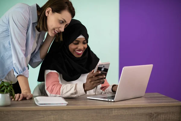 Afro woman with a hijab and a European woman using a smartphone and laptop in their home office. High quality photo
