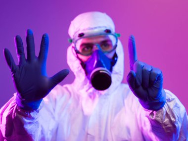 Coronavirus covid-19 salgını. Küresel sağlık salgını uyarısı ve mavi ve pembe neon ışıklı arka plandaki tehlike nedeniyle koruyucu biyolojik kıyafet ve maske giyen doktor.