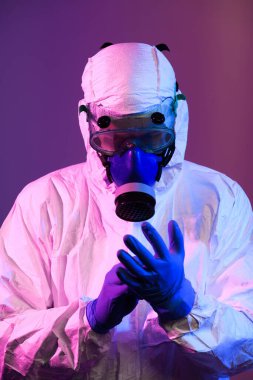 Coronavirus covid-19 salgını. Küresel sağlık salgını uyarısı ve mavi ve pembe neon ışıklı arka plandaki tehlike nedeniyle koruyucu biyolojik kıyafet ve maske giyen doktor.