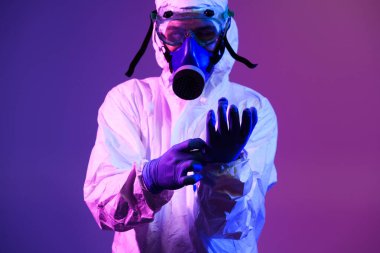 Coronavirus covid-19 salgını. Küresel sağlık salgını uyarısı ve mavi ve pembe neon ışıklı arka plandaki tehlike nedeniyle koruyucu biyolojik kıyafet ve maske giyen doktor.